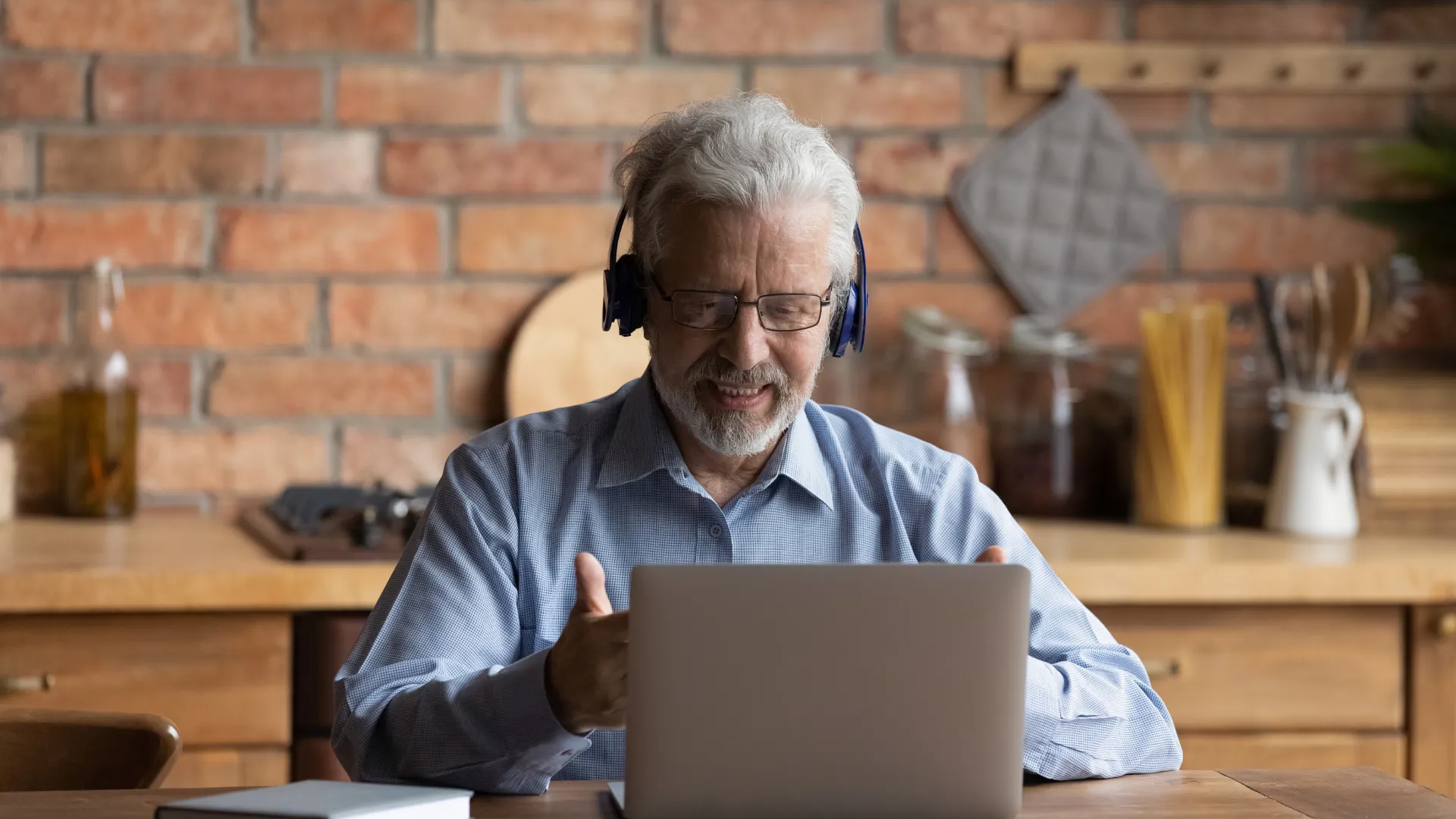 Ein Mann sitzt am Küchentisch am Laptop und trägt Kopfhörer, scheinbar in einem virtuellen Meeting.