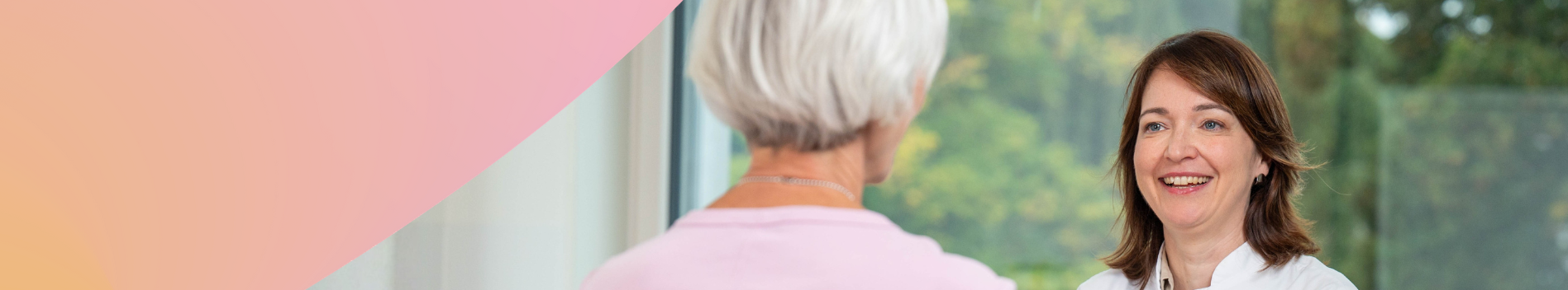 Ärztin im freundlichen Gespräch mit einer Patientin, die man nur von hinten sieht.