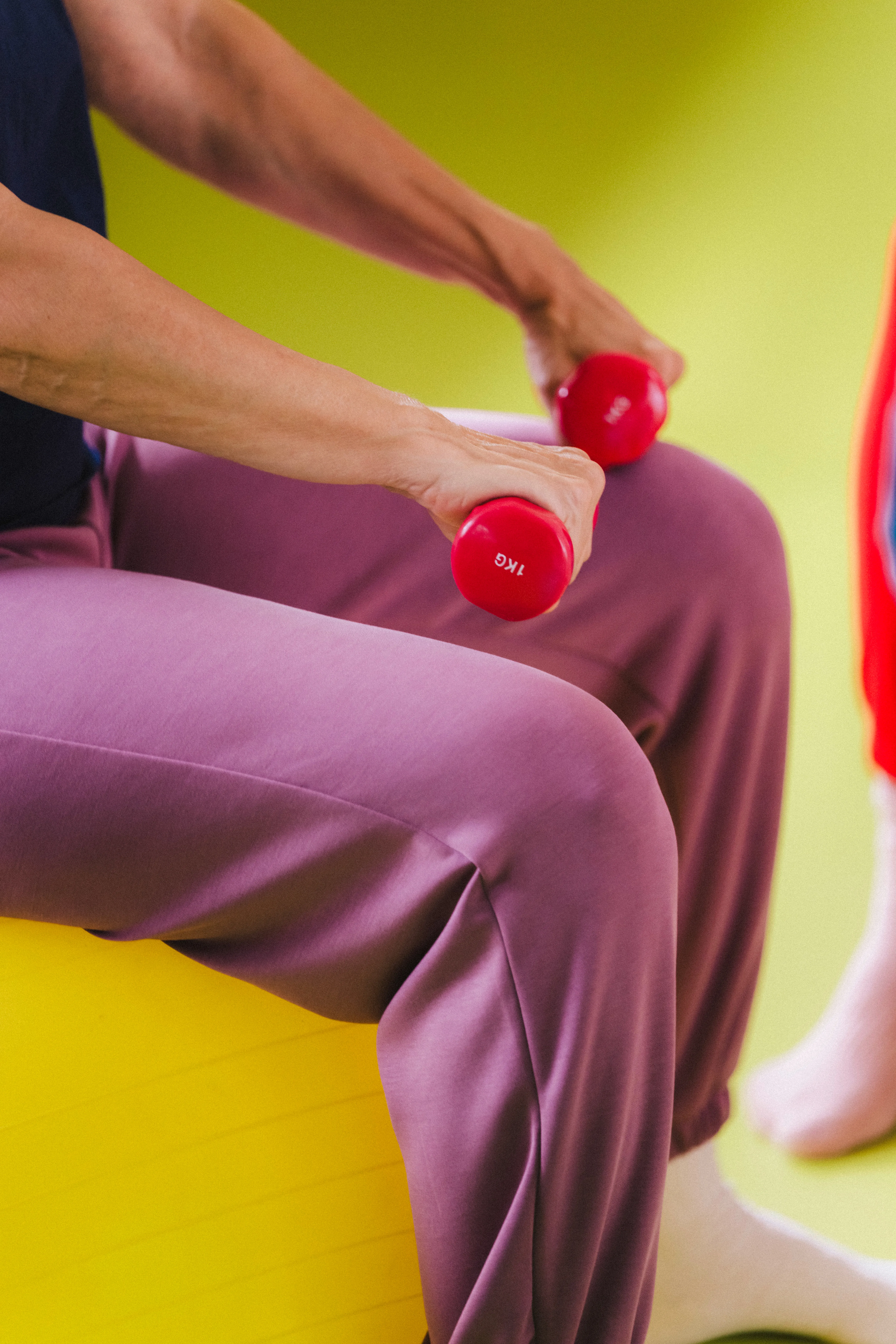 Person sitzt auf Gymnastikball und hält 2 Hanteln in den Häden.