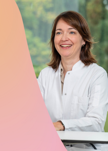 Ärztin freundlich lächelnd sitzt am Tisch und ist in ein Gespräch verwickelt.