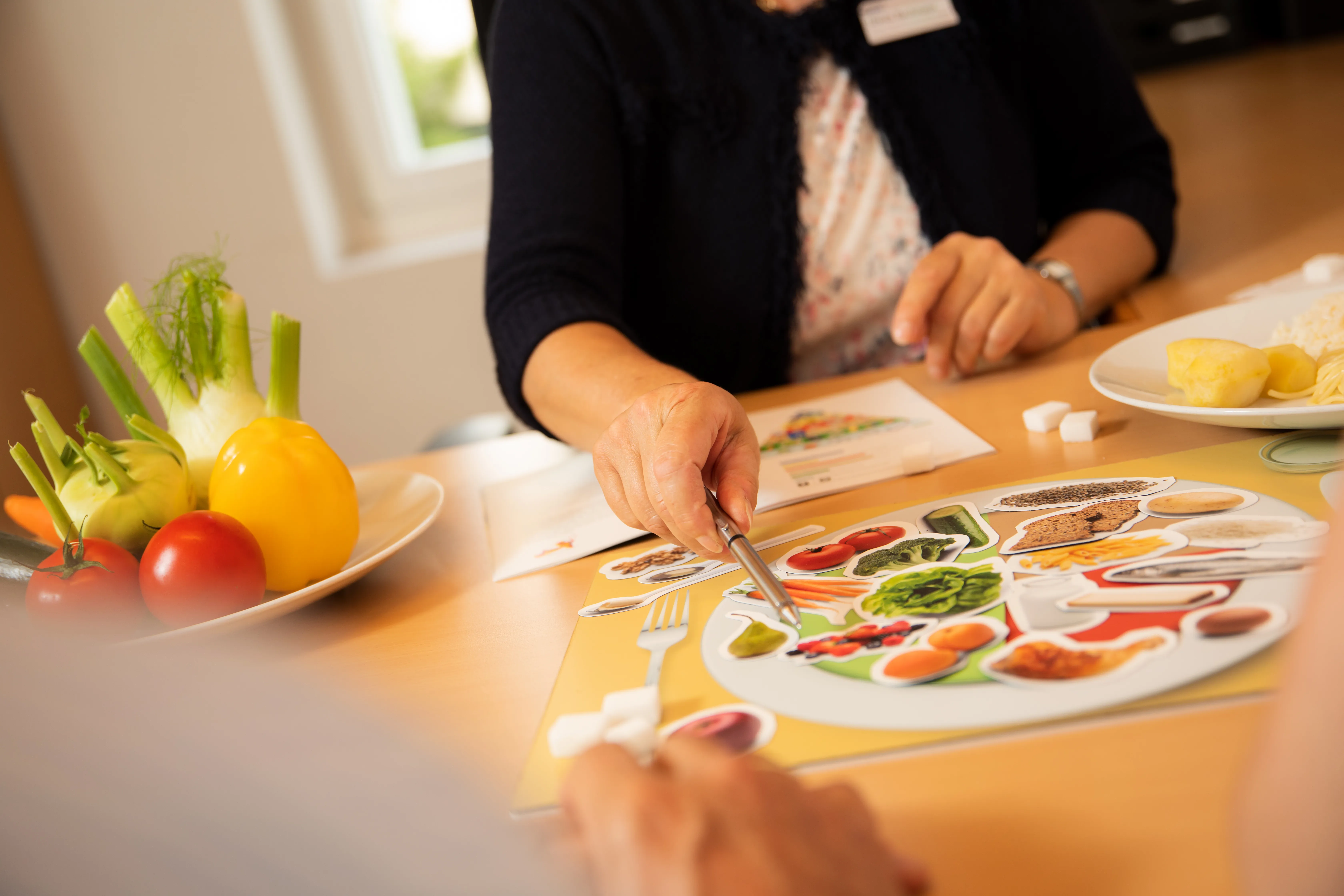 Nahaufnahme eines Bildes mit Nahrungsmittel und einer Ernährungsberaterin im Gespräch mit einem Patienten.