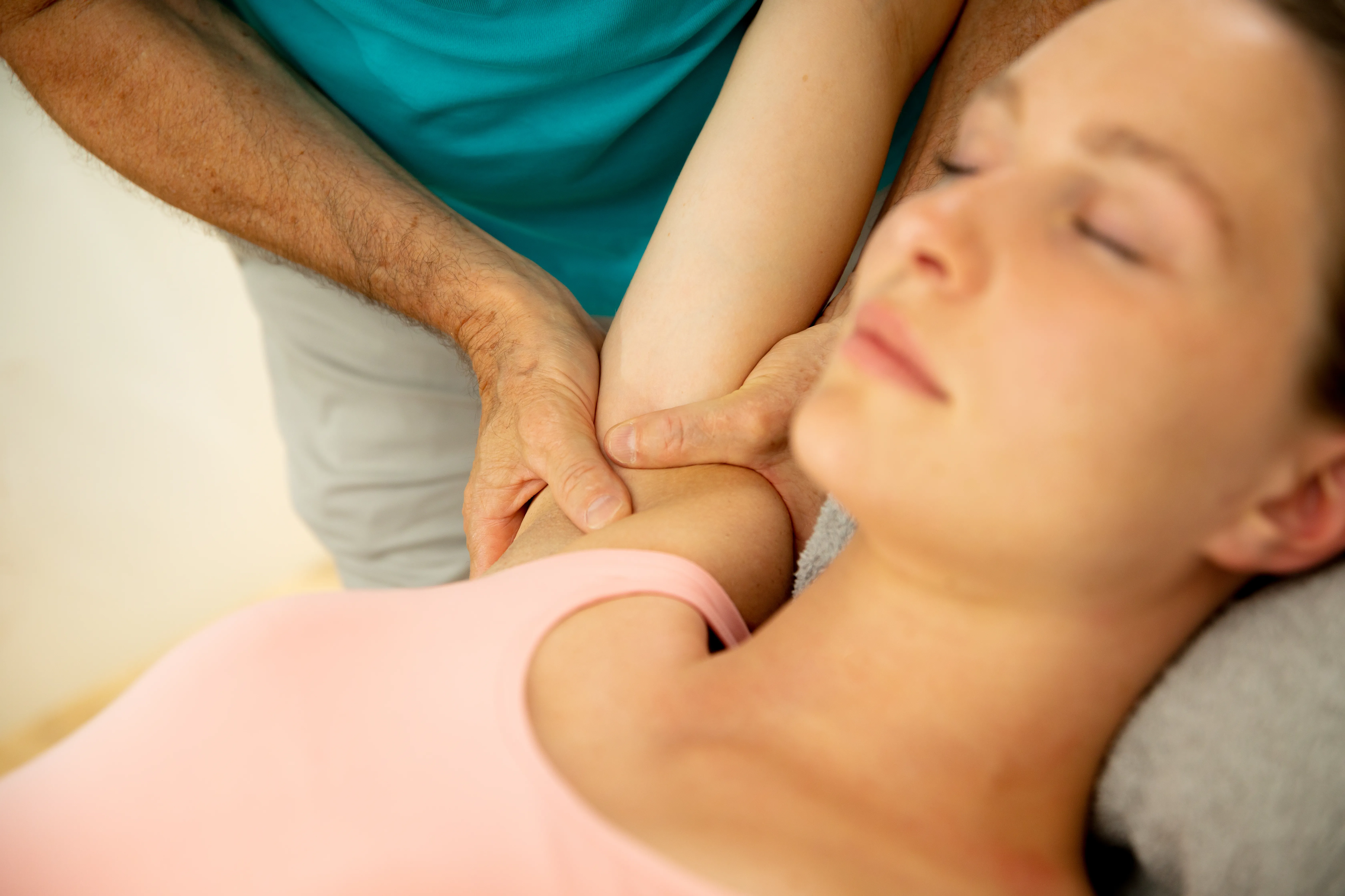Patientin liegt mit geschlossenen Augen und erhält Massage an den Schultern.
