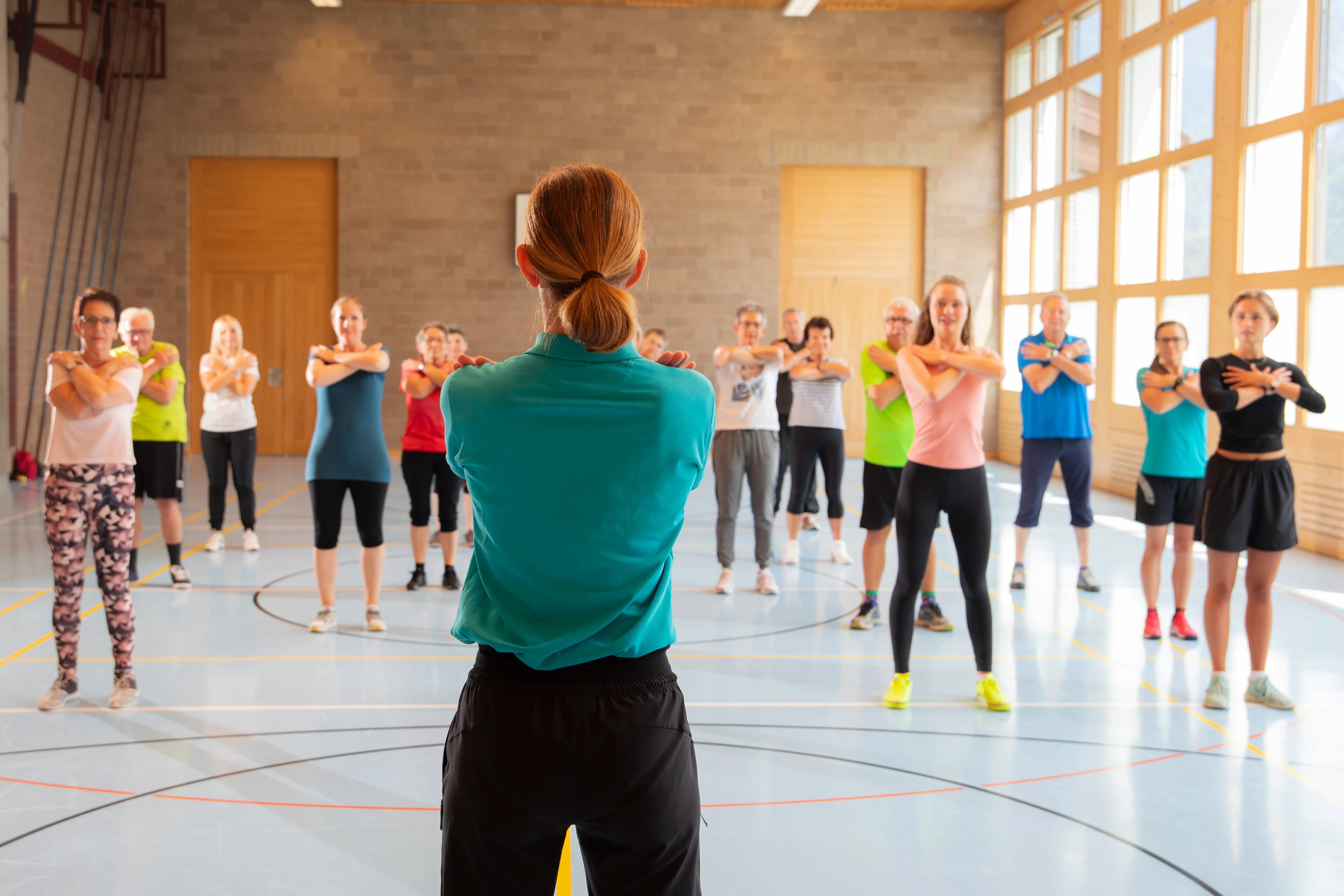 Ansicht einer Therapeutin von hinten mit einer grossen Gruppe von Patient:innen während einer Physiotherapie-Stunde.